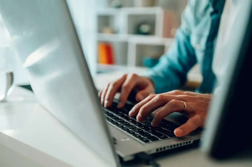 Close up of programmer's hands typing on laptop and coding.