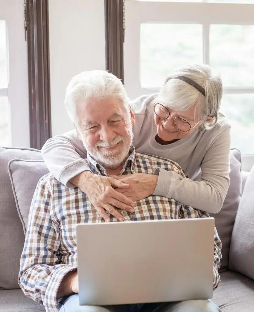 Happy white-haired 70-year-old couple at home using laptop together to shop online