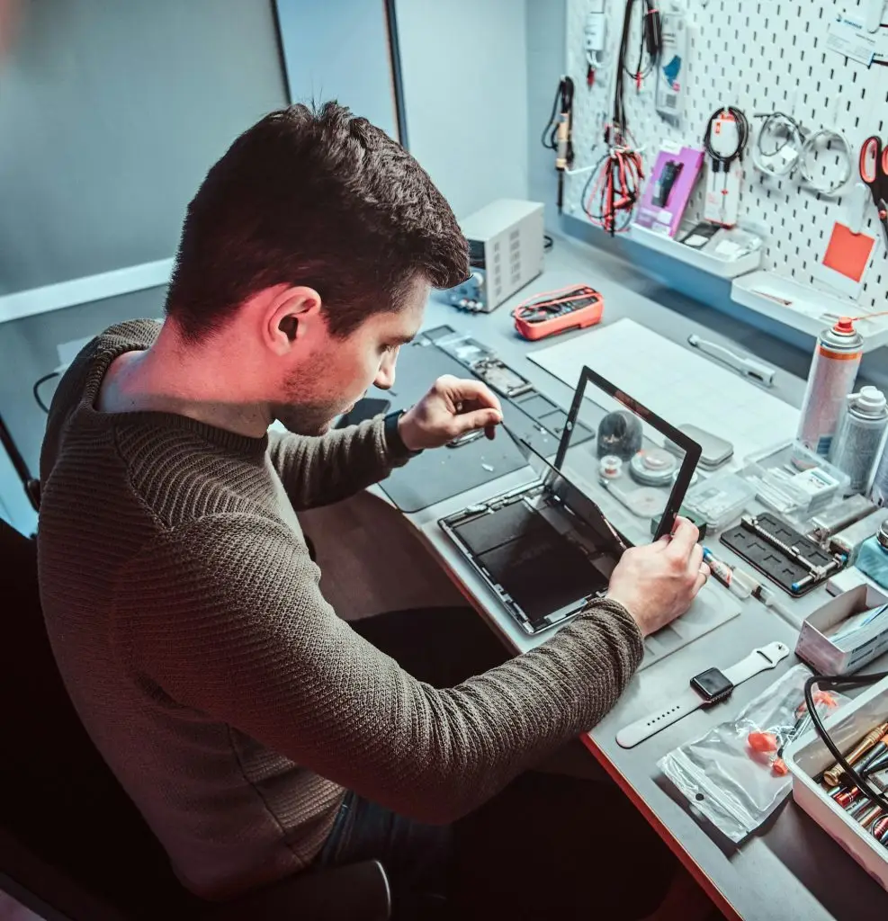 The technician repairs a broken tablet computer in a repair shop